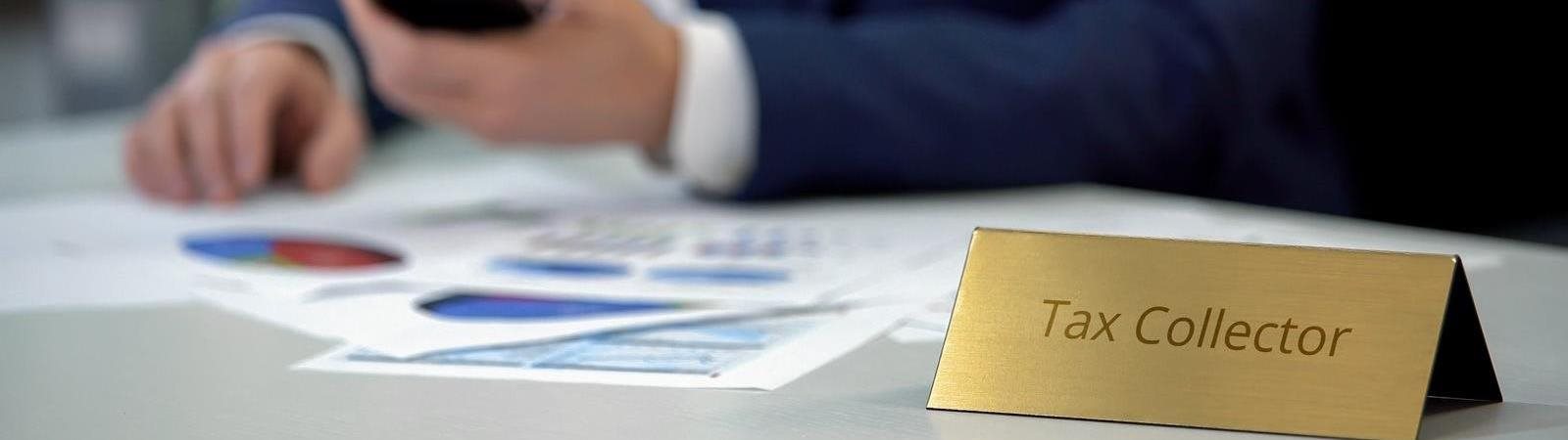 Man at Desk with Name Tag that says Tax Collector